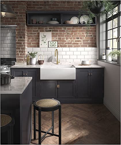 White fireclay farmhouse apron front sink with single bowl installed in dark cabinetry below white subway tile backsplash.