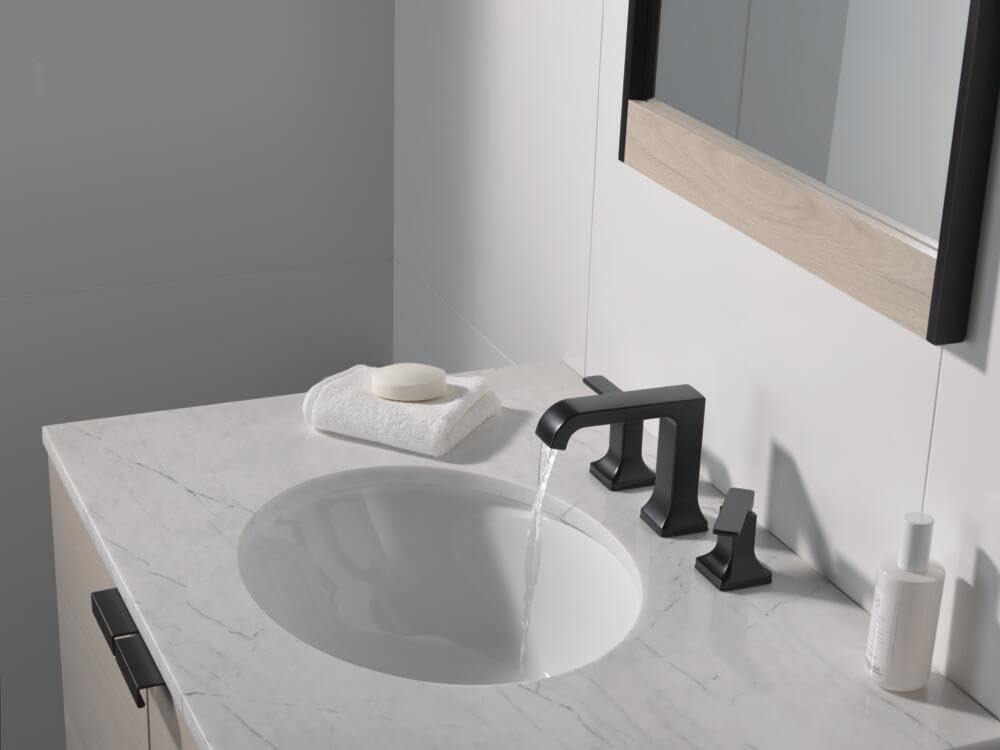 Matte black two-handle widespread faucet with angular spout installed on marble bathroom vanity with white undermount sink.