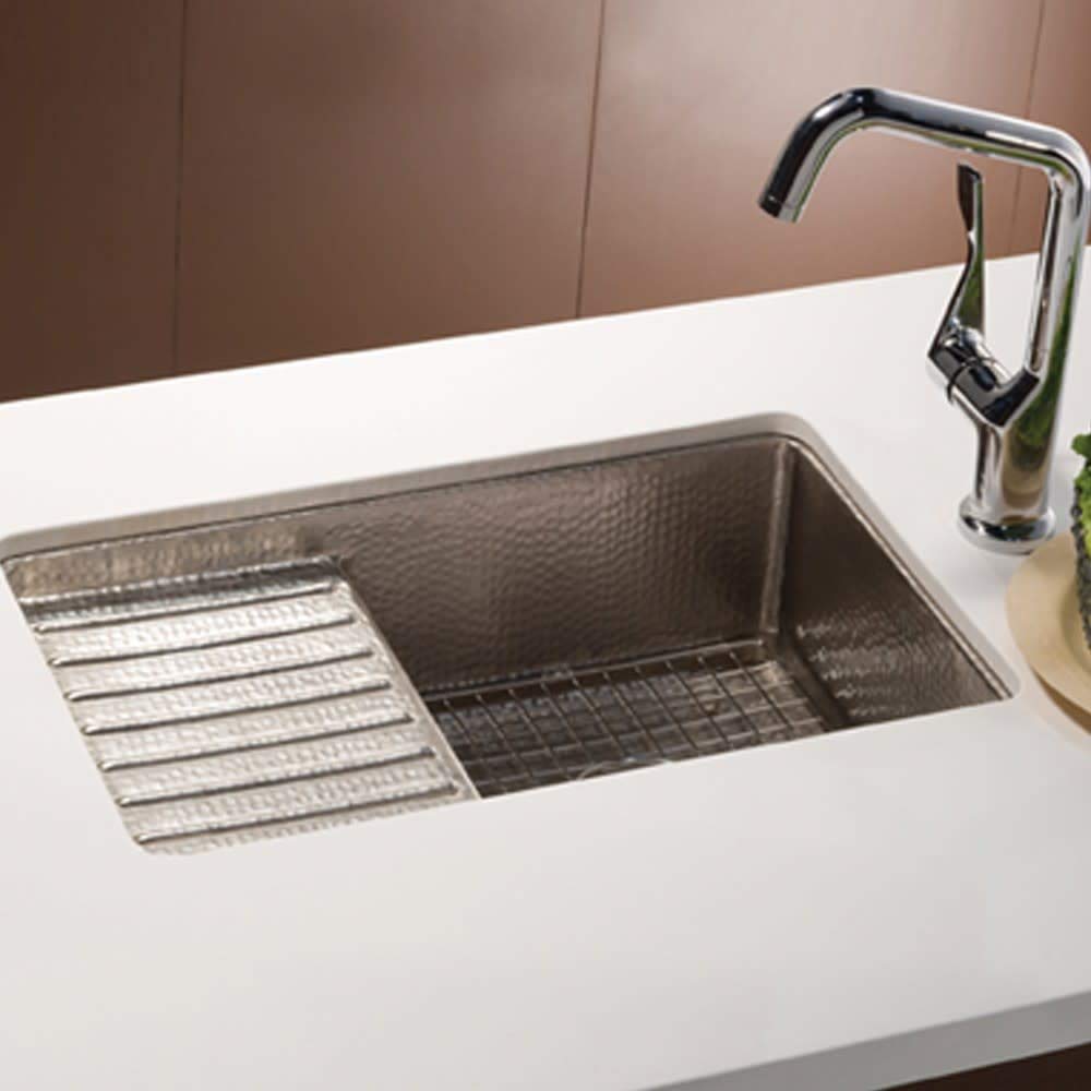 Hammered copper undermount sink with antique finish, grid strainer, and chrome faucet installed in white countertop.