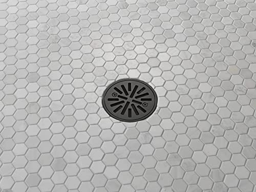 Matte black round shower drain with radial slots installed in hexagonal tile flooring.