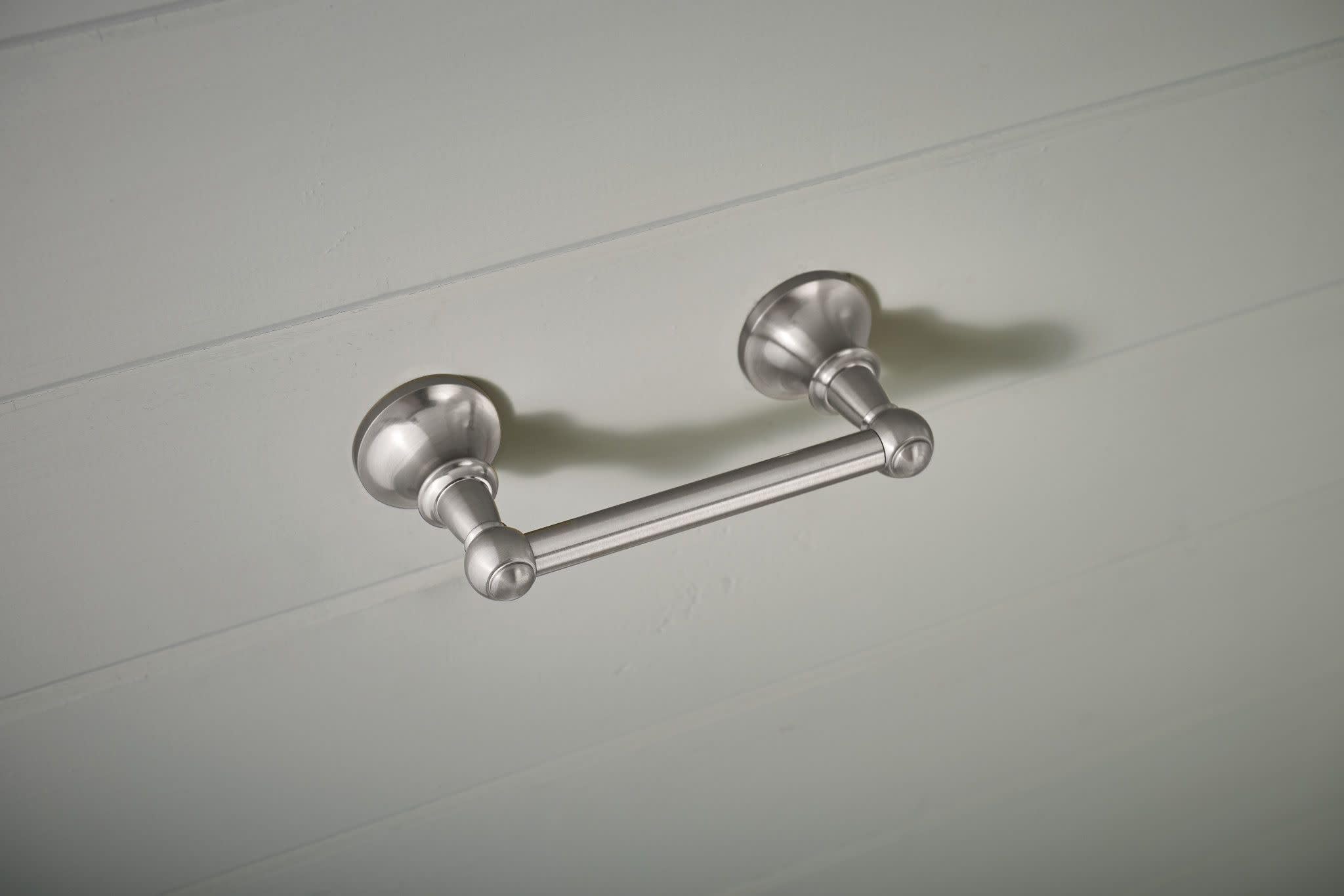 Brushed nickel pivoting toilet paper holder mounted on white wall with round finials and horizontal rod.