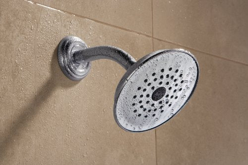 Chrome raincan shower head mounted on tiled wall with curved arm and circular face with spray holes.