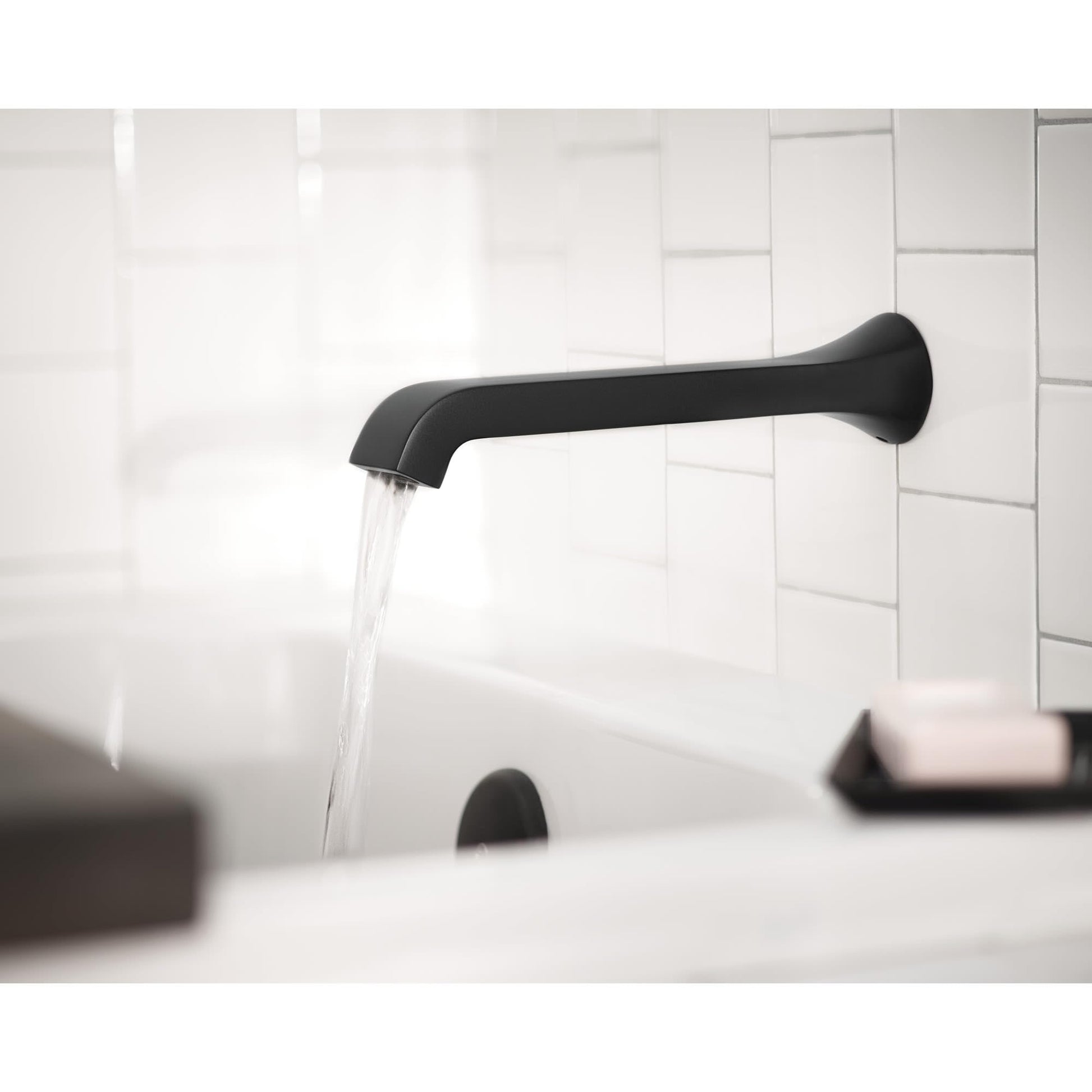 Chrome wall-mounted tub faucet with single handle and curved spout dispensing water into bathtub.