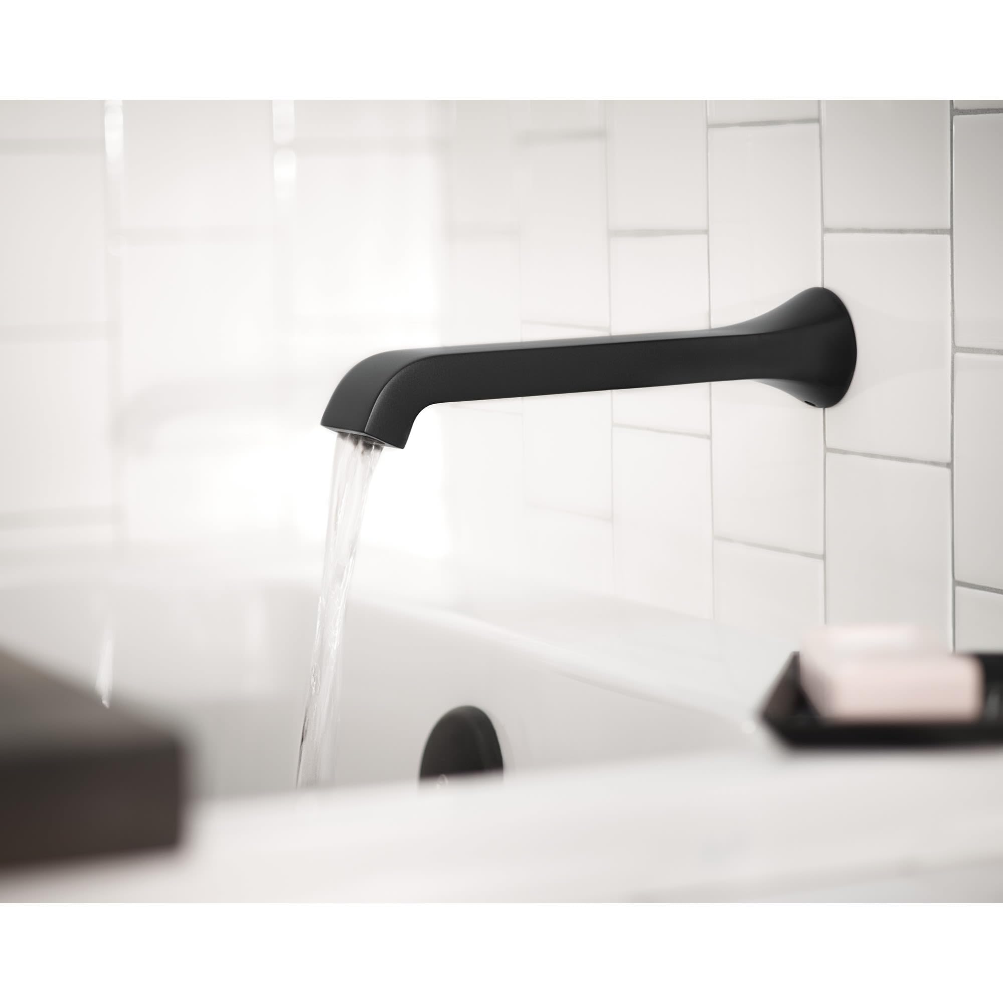 Chrome wall-mounted tub faucet with single handle and curved spout dispensing water into bathtub.