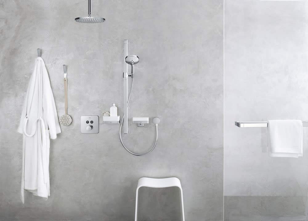Chrome soap dispenser with shelf mounted on gray tile bathroom wall next to shower fixtures.