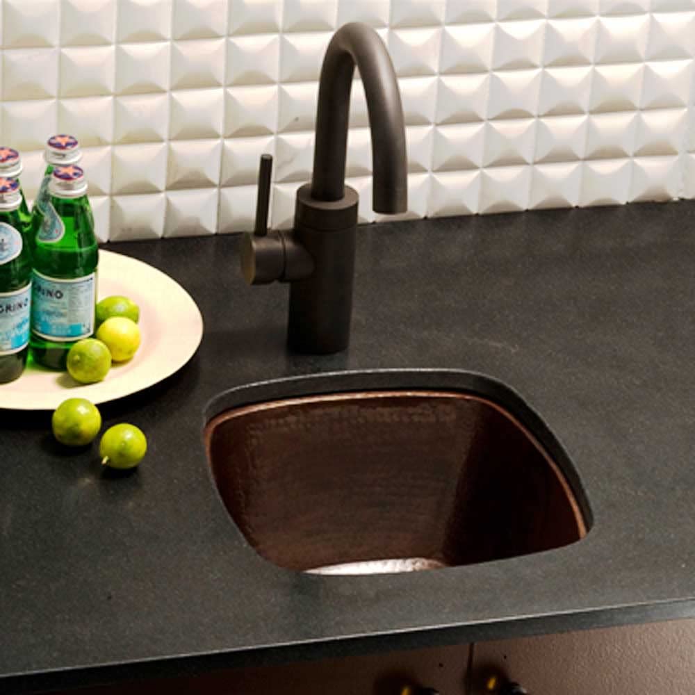 Small square hammered copper sink with dark finish installed in countertop, paired with black curved faucet.