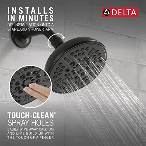 Matte black round shower head with multiple spray holes and adjustable spray arm mounted on white tile wall.