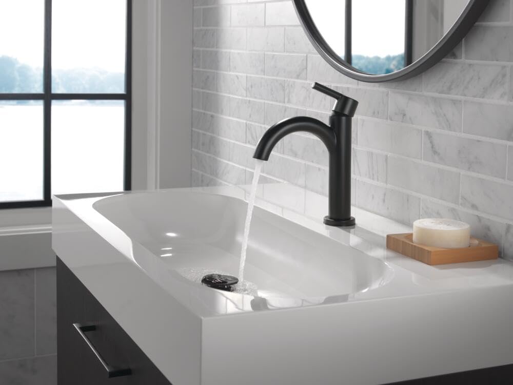 Matte black single-handle bathroom faucet with curved spout installed above white sink with running water.