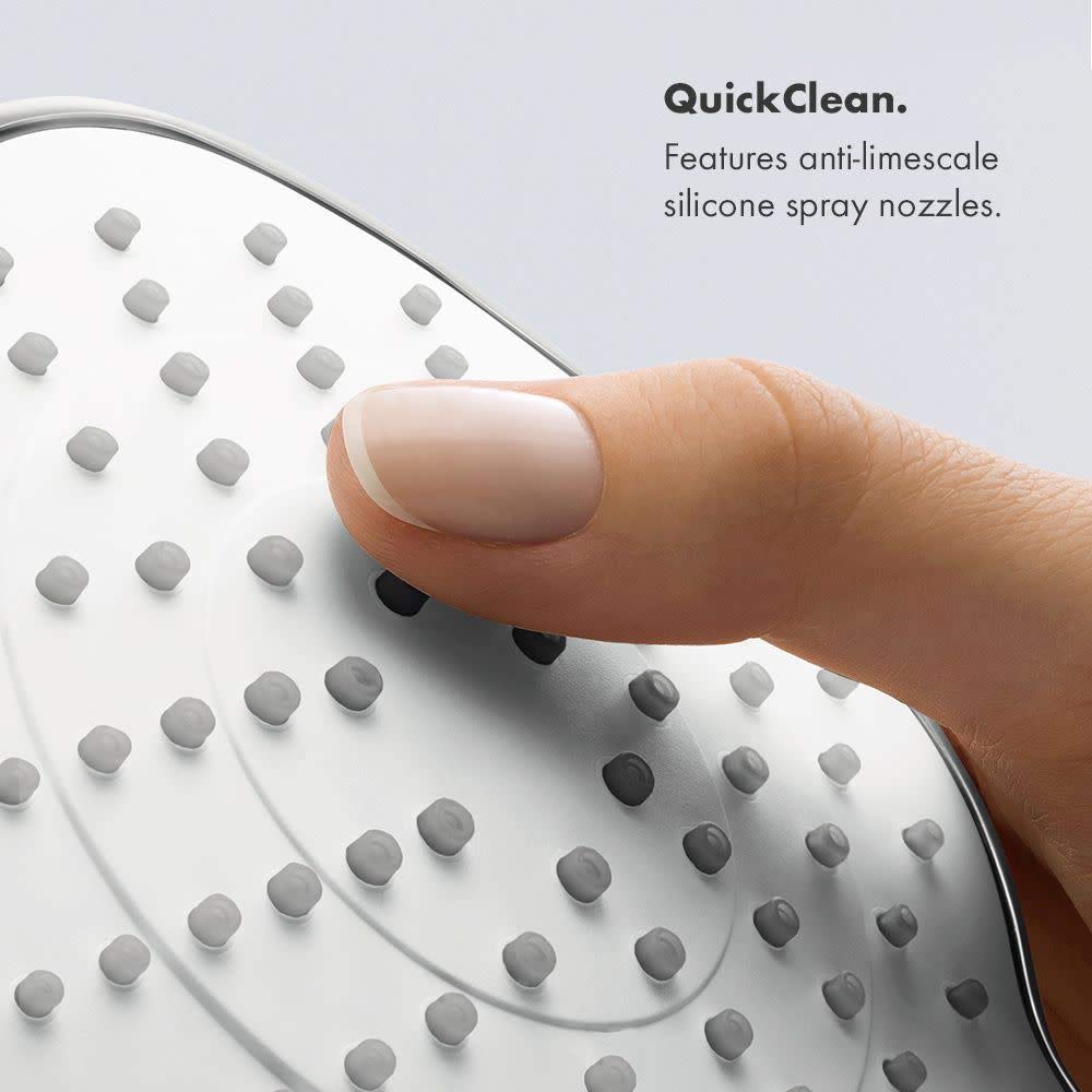 Brushed nickel round shower head with multiple spray nozzles, finger touching surface to demonstrate cleaning feature.