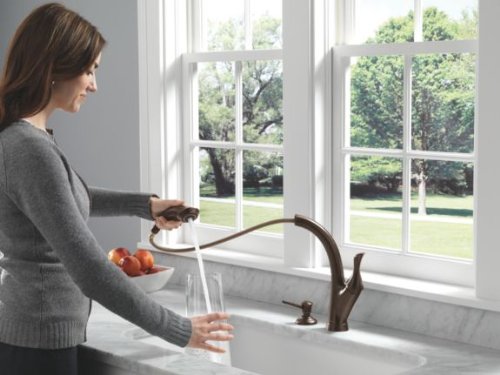 Venetian bronze soap and lotion dispenser mounted on kitchen sink counter with woman using it.