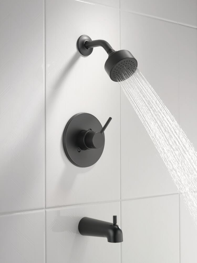 Matte black tub and shower trim with round showerhead, curved arm, circular valve trim, and tub spout on white tile wall.