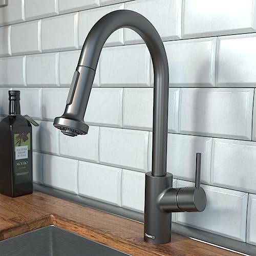 Brushed black chrome kitchen faucet with curved spout and pull-down spray head mounted above sink with white subway tile back