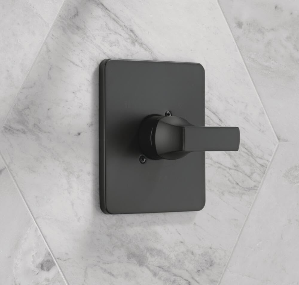 Matte black shower valve trim with rectangular escutcheon plate and lever handle mounted on marble tile.
