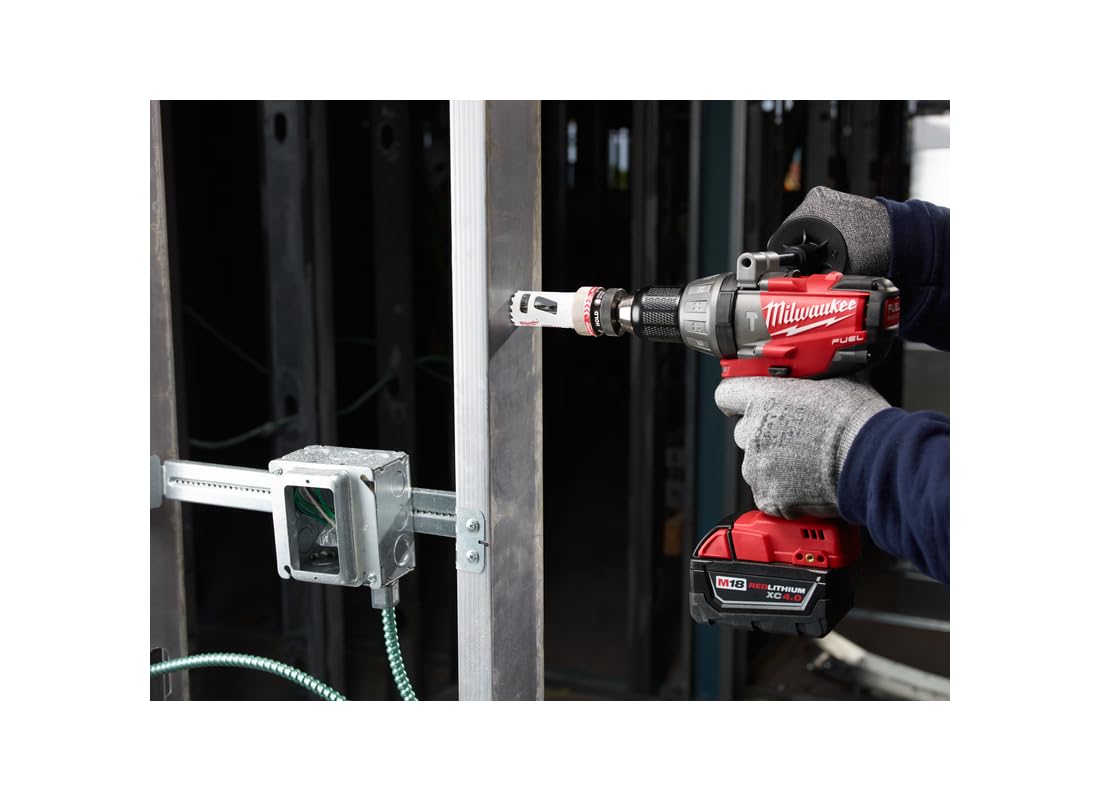 Milwaukee 2-1/4" bi-metal hole saw attached to red drill with battery, cutting into metal framing.