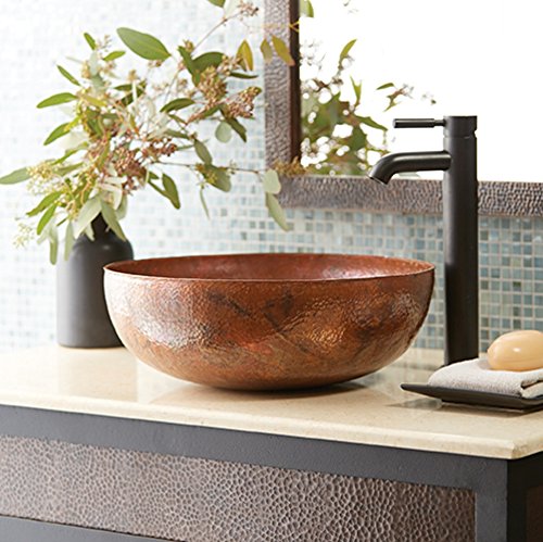 Round hammered copper vessel sink with textured finish on bathroom countertop with black faucet.