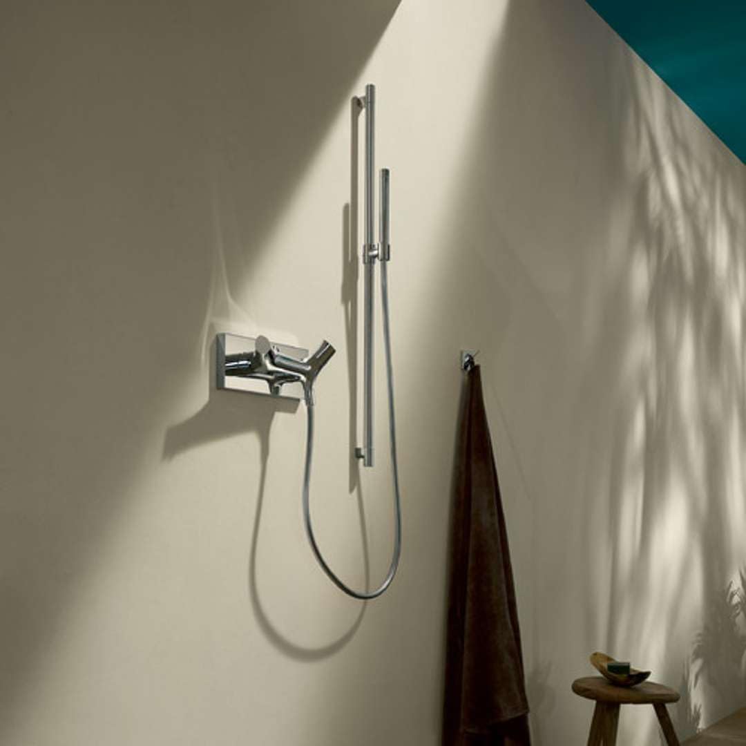 Chrome wallbar mounted on white bathroom wall with handheld showerhead and hose attached.