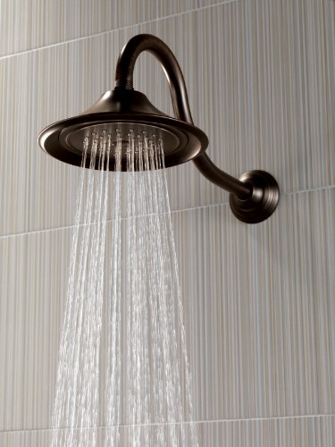 Venetian bronze shower head with curved arm and wide circular face mounted on tiled wall.