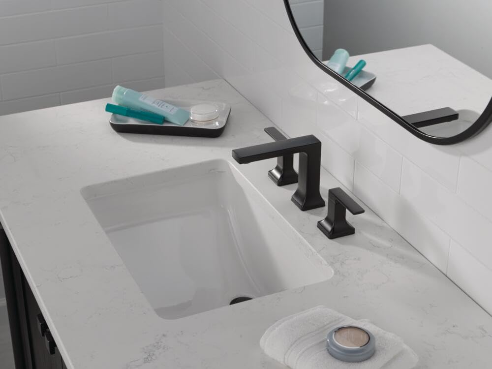 Matte black two-handle widespread bathroom faucet installed on white marble countertop above rectangular sink.