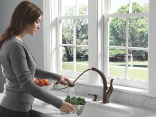 Venetian bronze soap and lotion dispenser mounted on white kitchen countertop near sink.