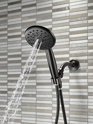 Oil rubbed bronze hand shower with circular perforated face mounted on wall with flexible hose and water stream visible.