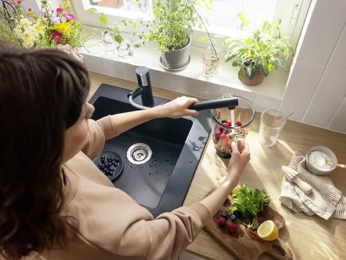 Matte black pull-out kitchen faucet with spray head extended over sink basin.