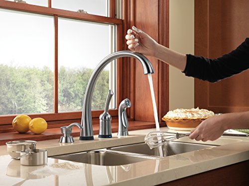 Stainless steel kitchen faucet with soap dispenser mounted on countertop sink.