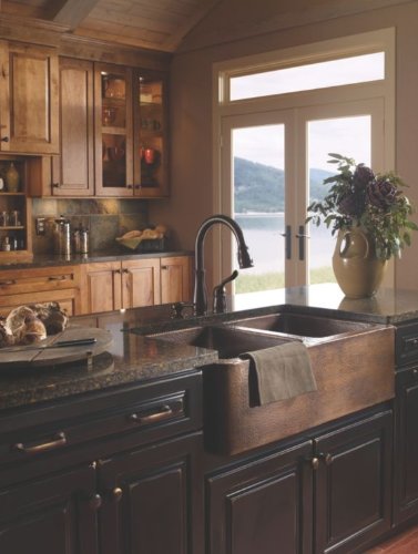 Venetian bronze soap dispenser mounted on dark kitchen countertop next to farmhouse sink.