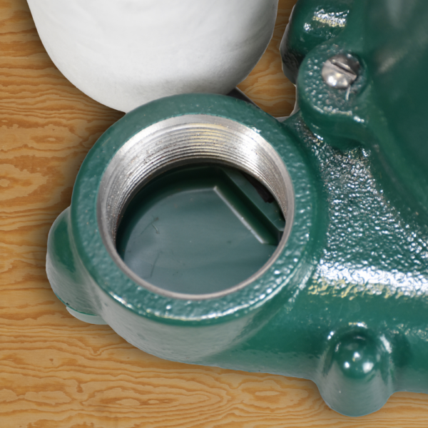 Green cast iron sump pump housing with threaded outlet connection and white float switch on wooden surface.