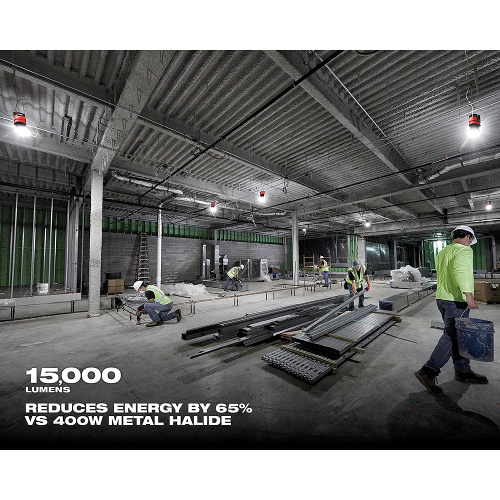 Milwaukee LED site light mounted on ceiling illuminating industrial warehouse with workers in safety gear and construction ma