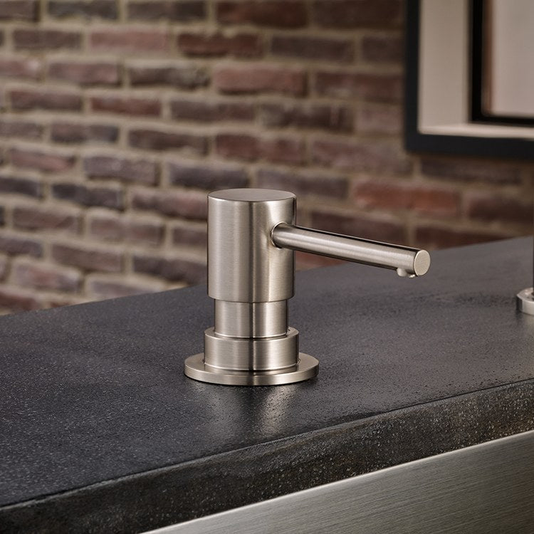 Chrome soap dispenser with cylindrical pump and round base mounted on dark countertop.