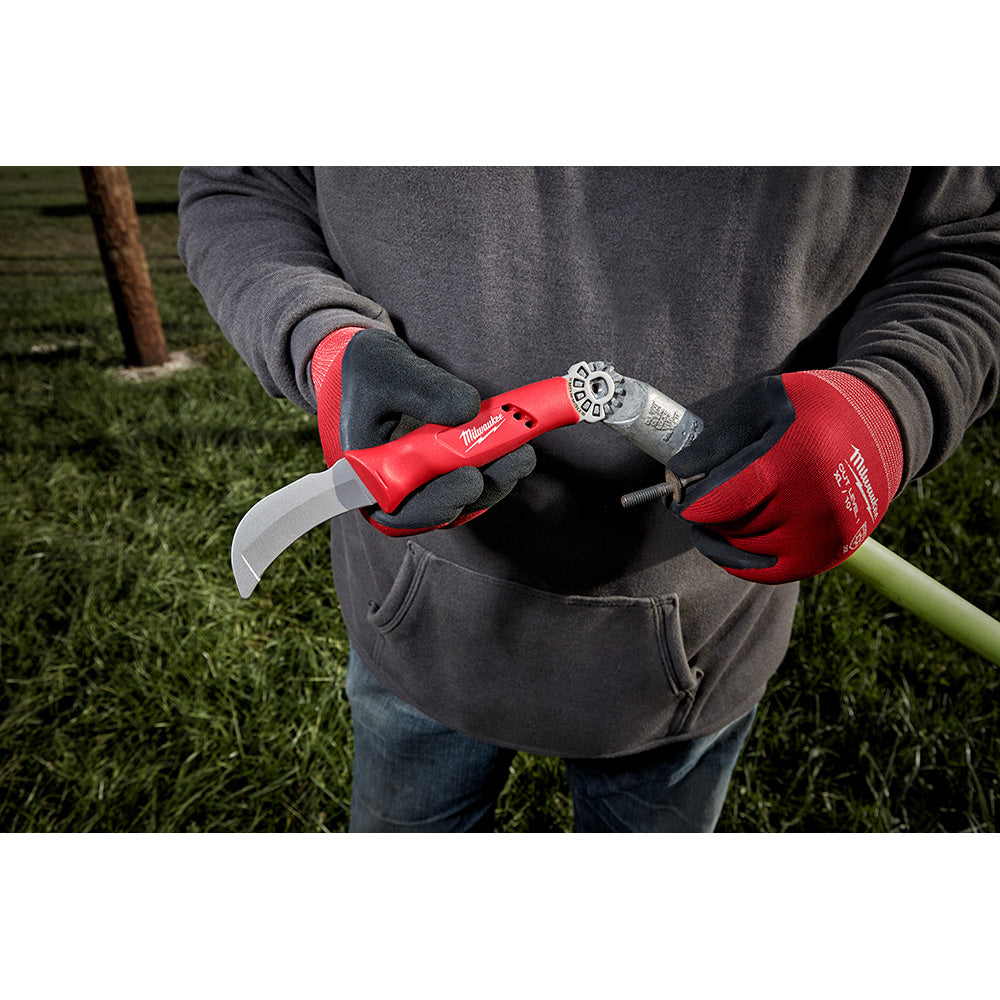 Red and black lineman knife with blunt curved blade and metal ring attachment, held in red gloved hand.