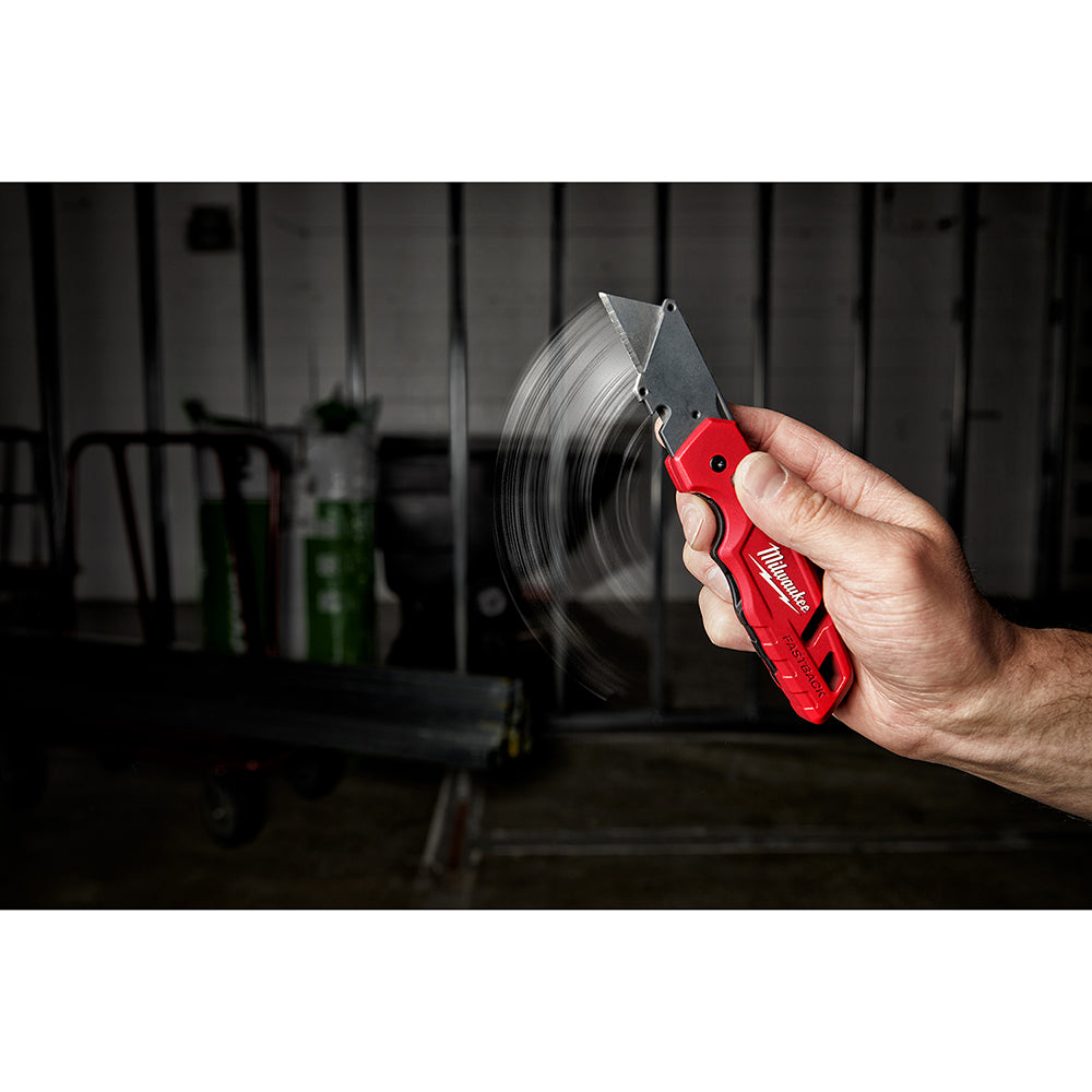 Red and black utility knife with curved blade held in hand with storage wheel visible in background.