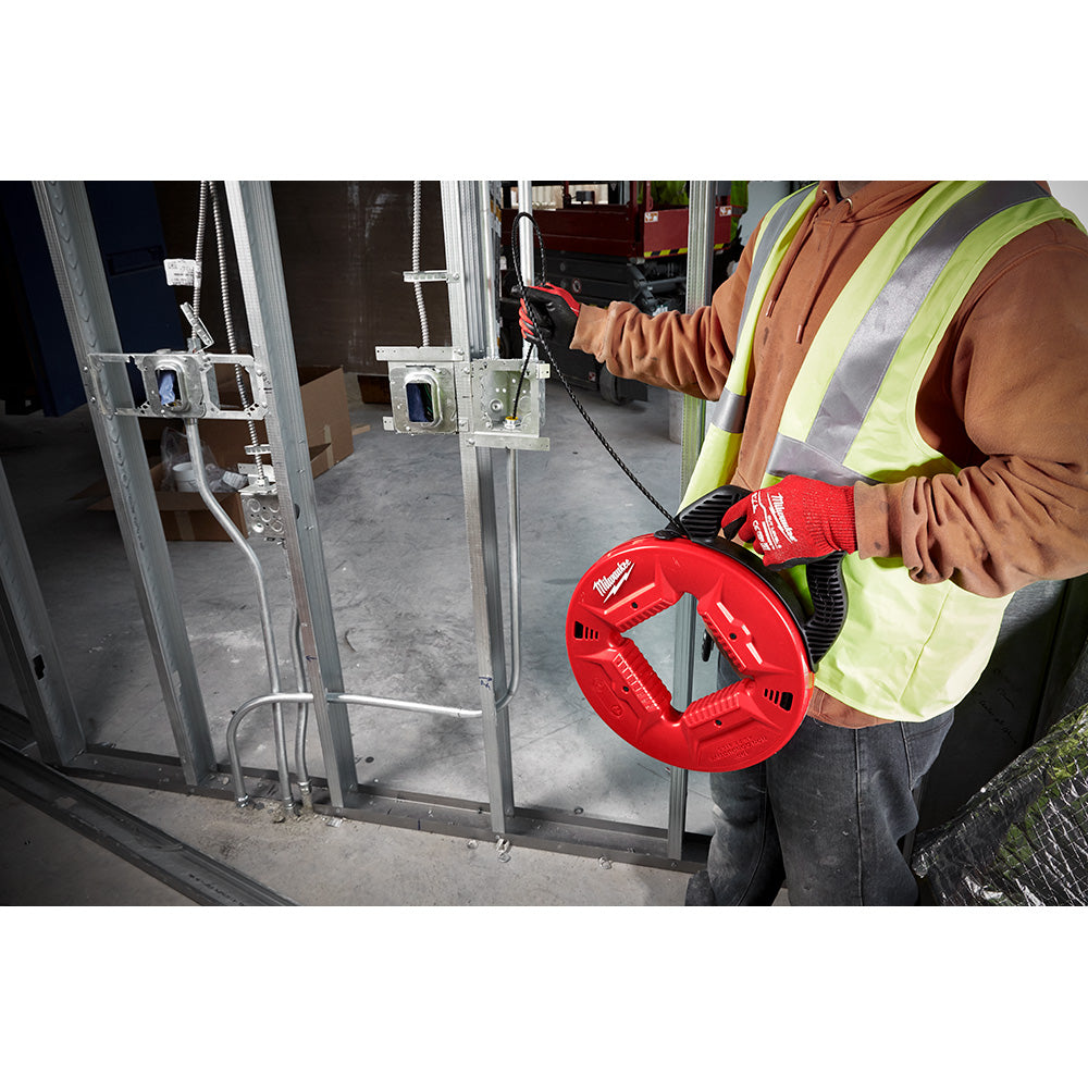 Worker in safety vest holding red Milwaukee fish tape reel with black cord near electrical conduit.