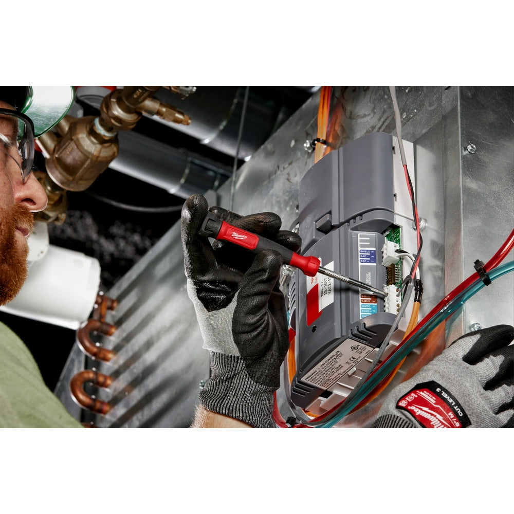 Red and black multi-bit screwdriver with interchangeable bits held in gloved hand during electrical work.