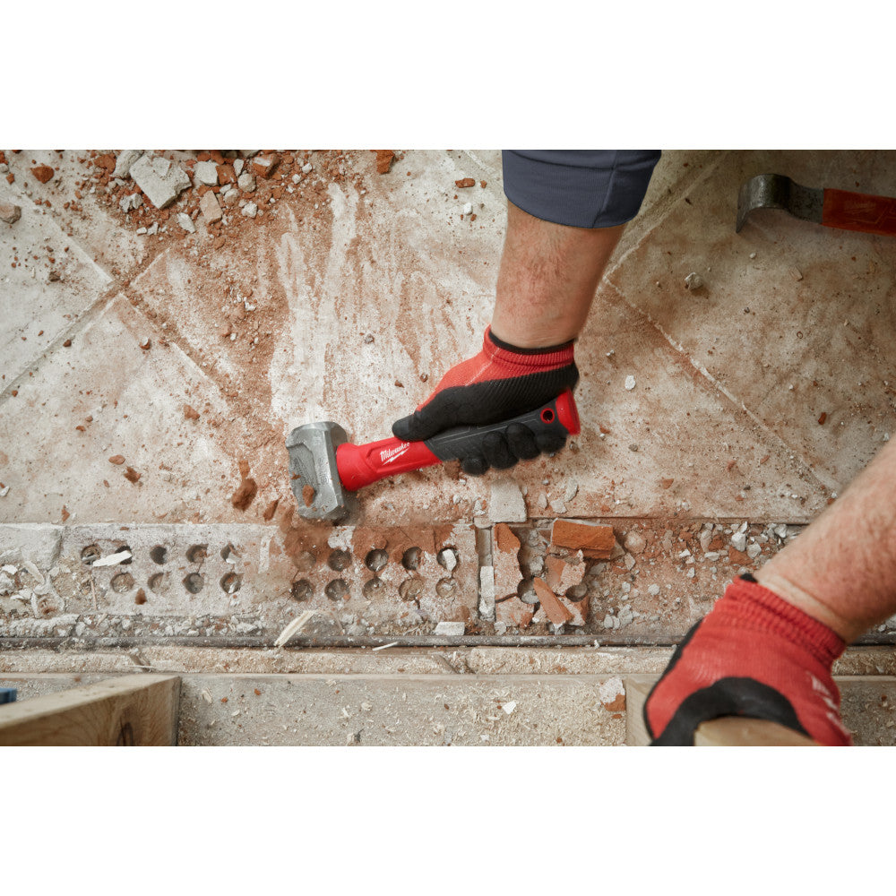 Milwaukee drilling hammer with red grip being used on concrete surface by person wearing work gloves.