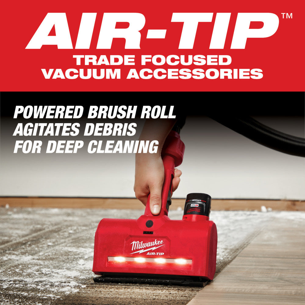 Red Milwaukee M12 AIR-TIP utility nozzle with powered brush roll and LED lights, held in hand above dusty surface.