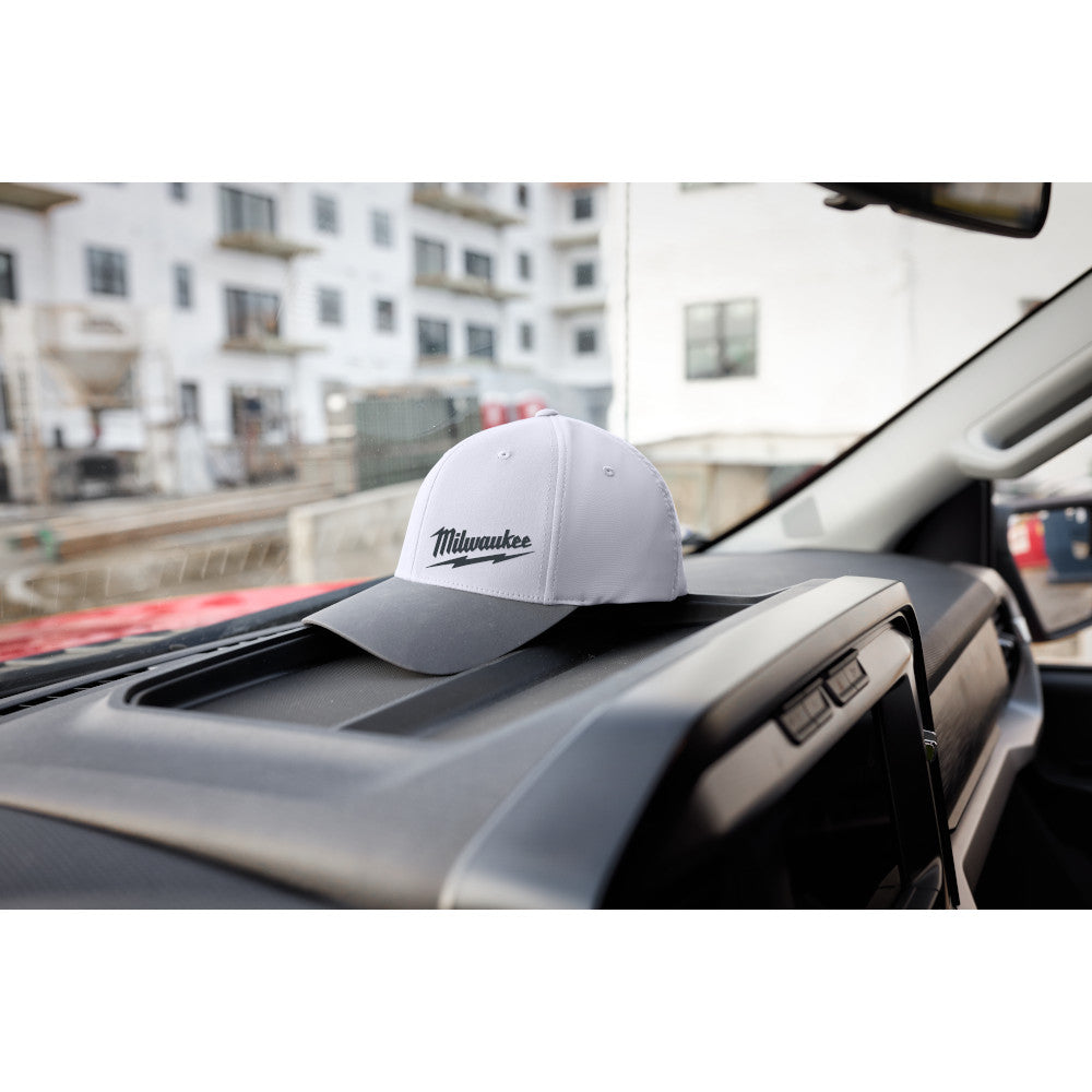 Gray and white fitted baseball cap with Milwaukee logo on front, displayed on vehicle dashboard.