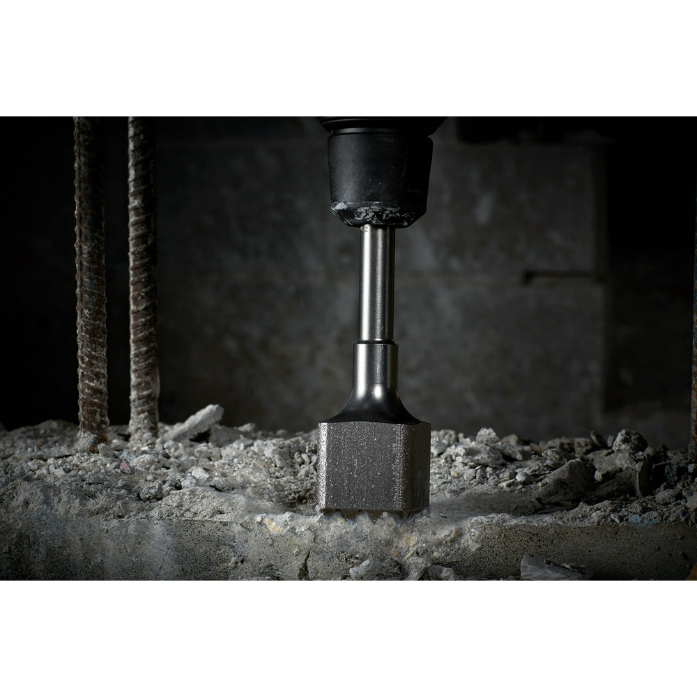 SDS-Max demolition bushing tool with square bit inserted into concrete surface surrounded by debris.