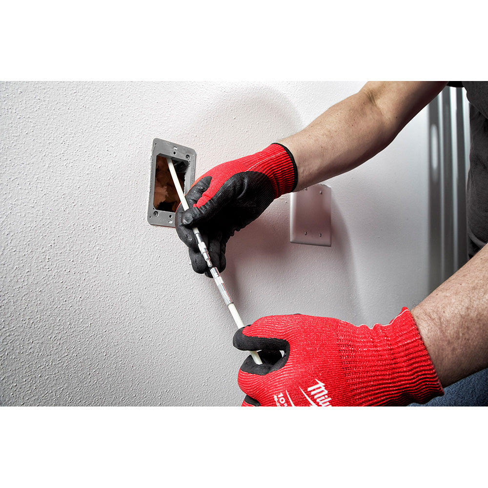 Person wearing red and black gloves using a white fish stick tool to route wire through a wall electrical box.
