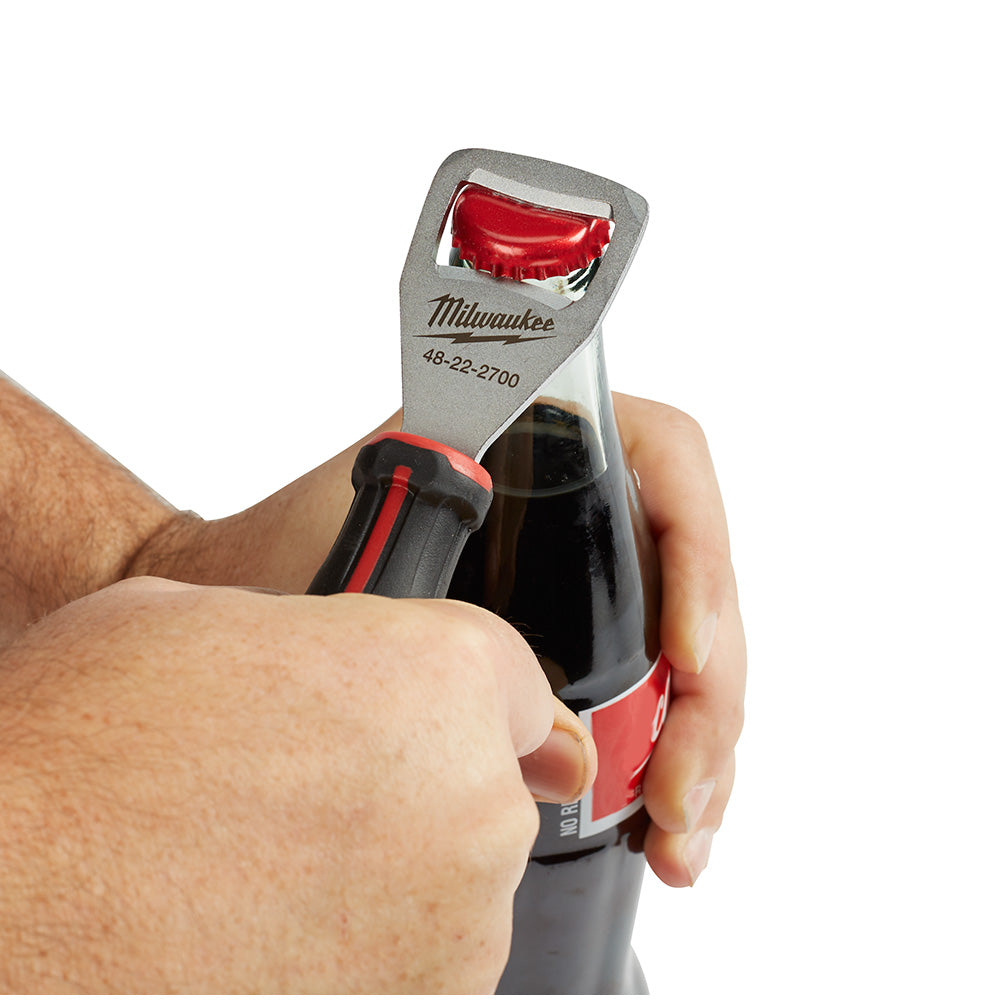 Milwaukee bottle opener with gray metal head and red rubberized handle, shown opening a dark bottle.
