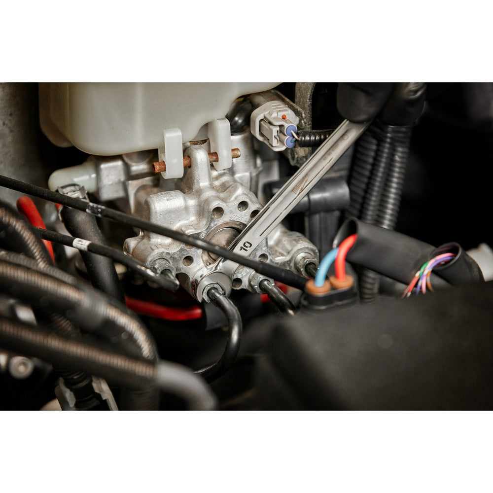 Metal double-end flare nut wrench with 13mm and 14mm openings installed on automotive hydraulic fitting.