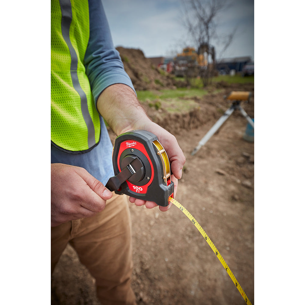 Person holding red and black Milwaukee closed reel tape measure with yellow measuring tape extended in outdoor construction s