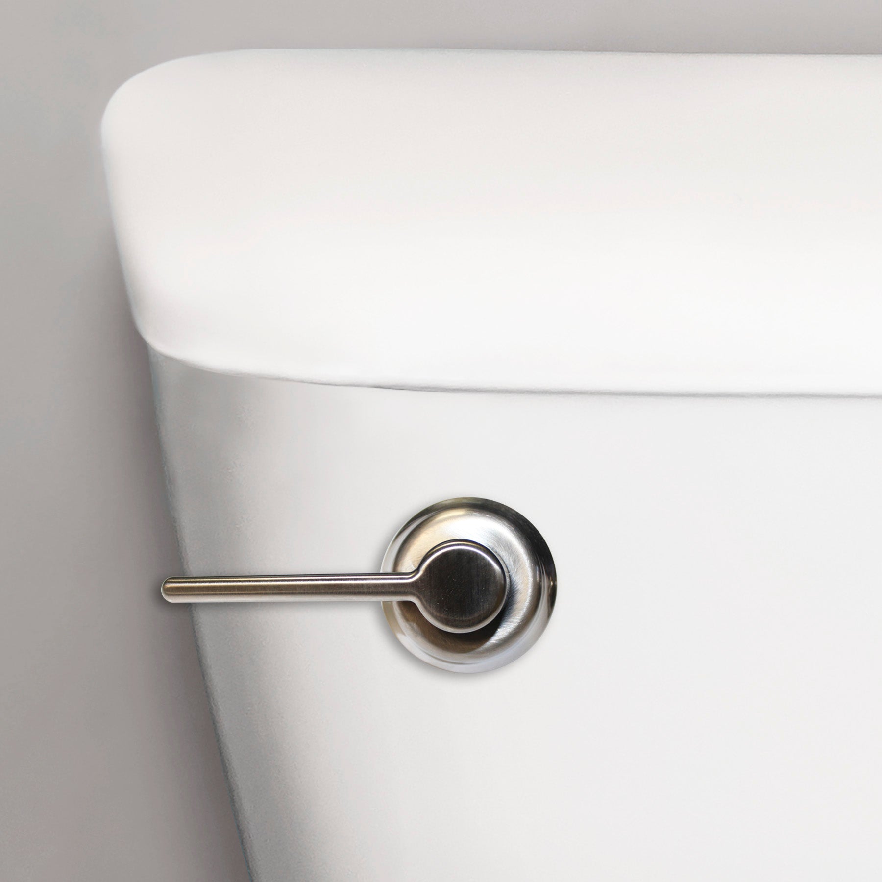 Brushed nickel toilet lever handle mounted on white ceramic tank.