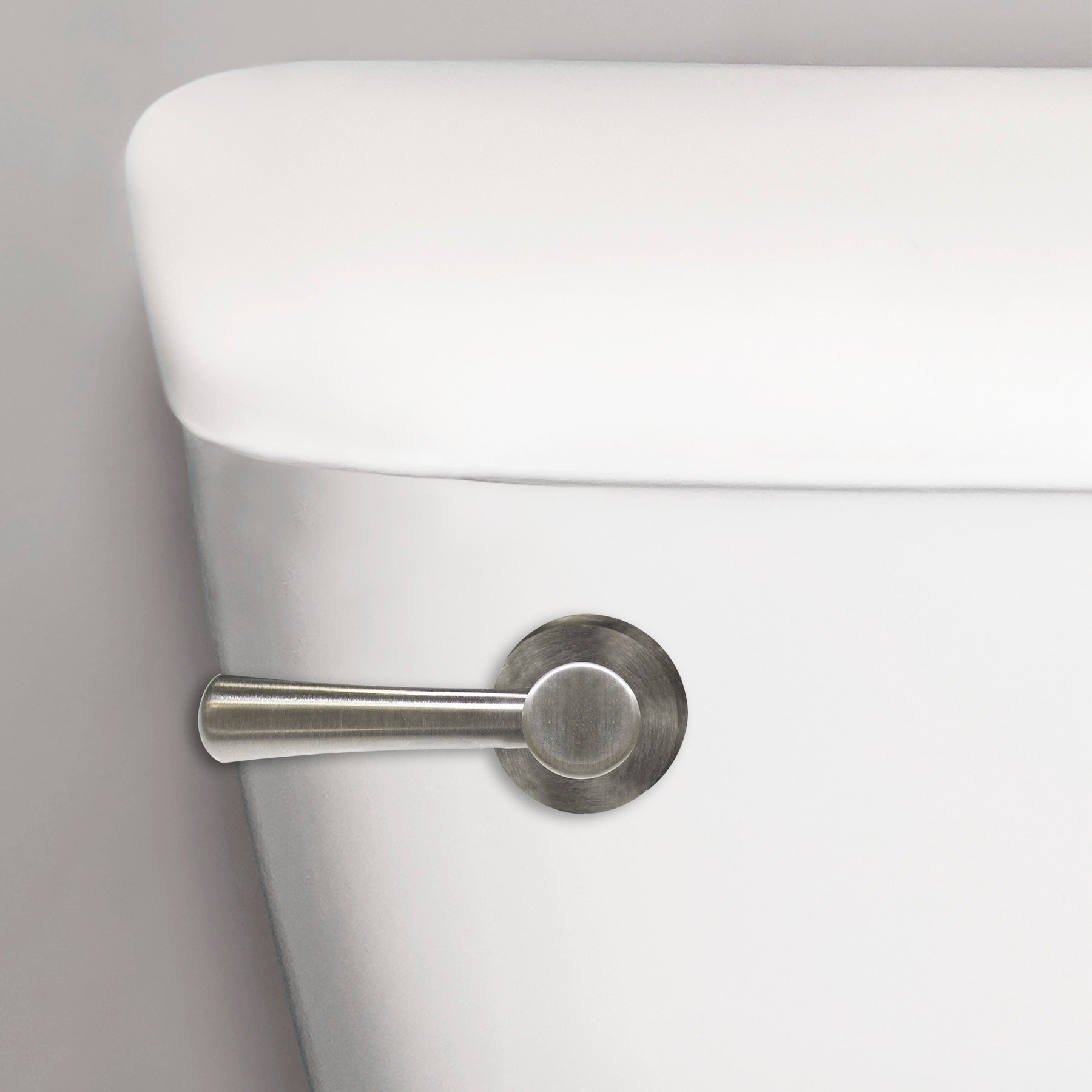 Brushed nickel toilet handle with cylindrical lever mounted on white porcelain tank.