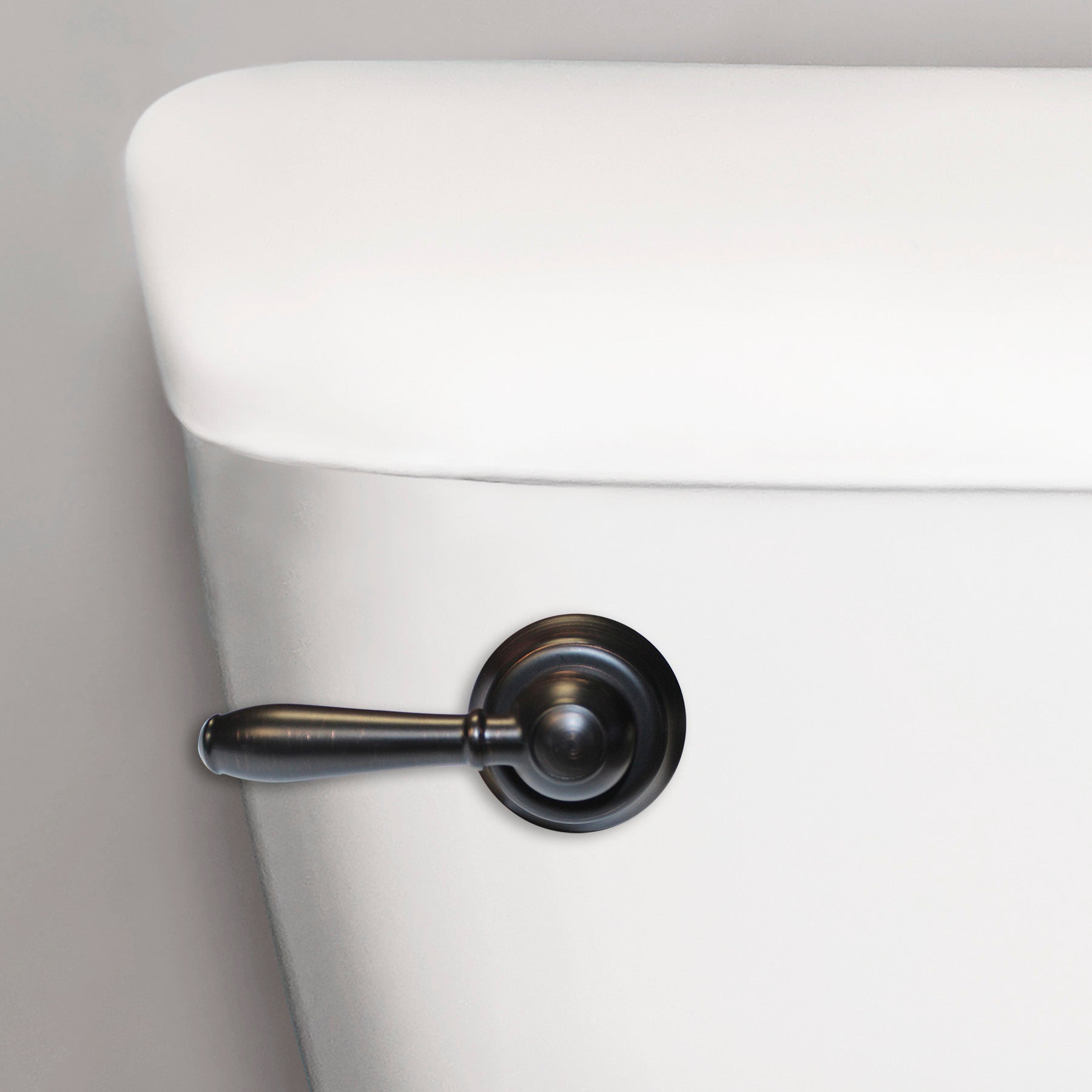 Oil rubbed bronze toilet handle lever mounted on white porcelain tank.