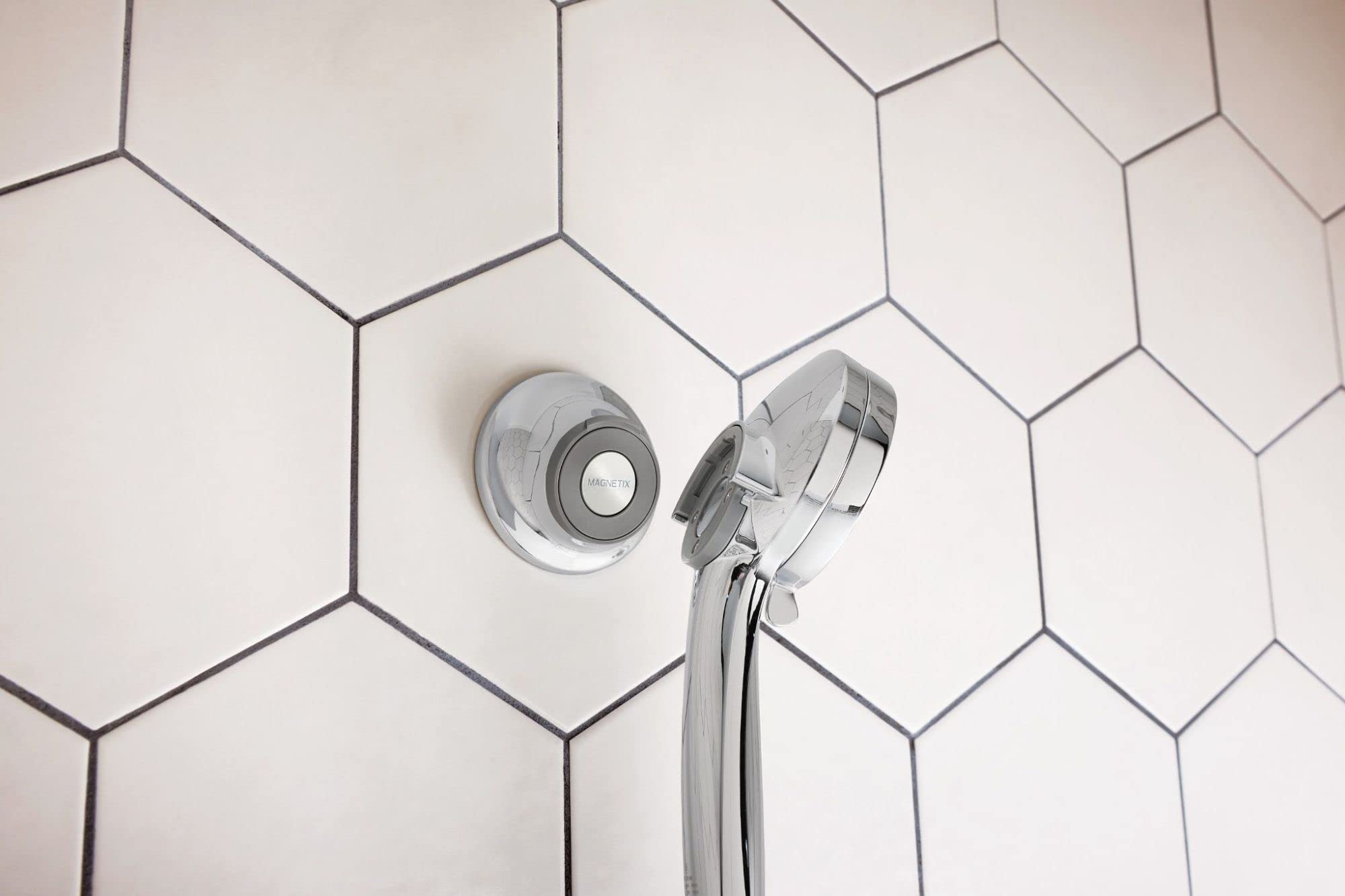 Chrome magnetic cradle mounted on white hexagonal tile wall with showerhead holder and hose attachment.