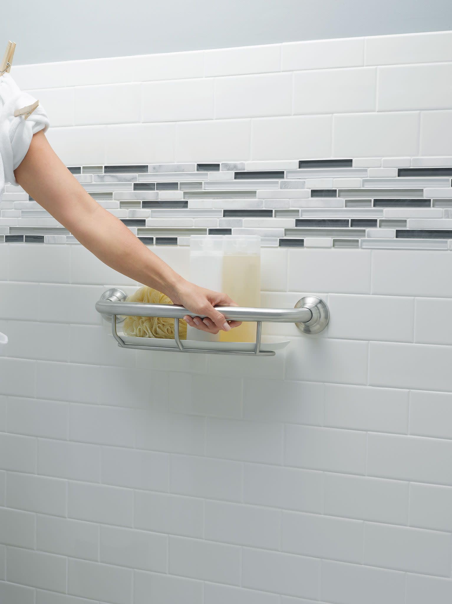 Chrome grab bar with integrated shelf holding bathroom items, mounted on white subway tile wall.