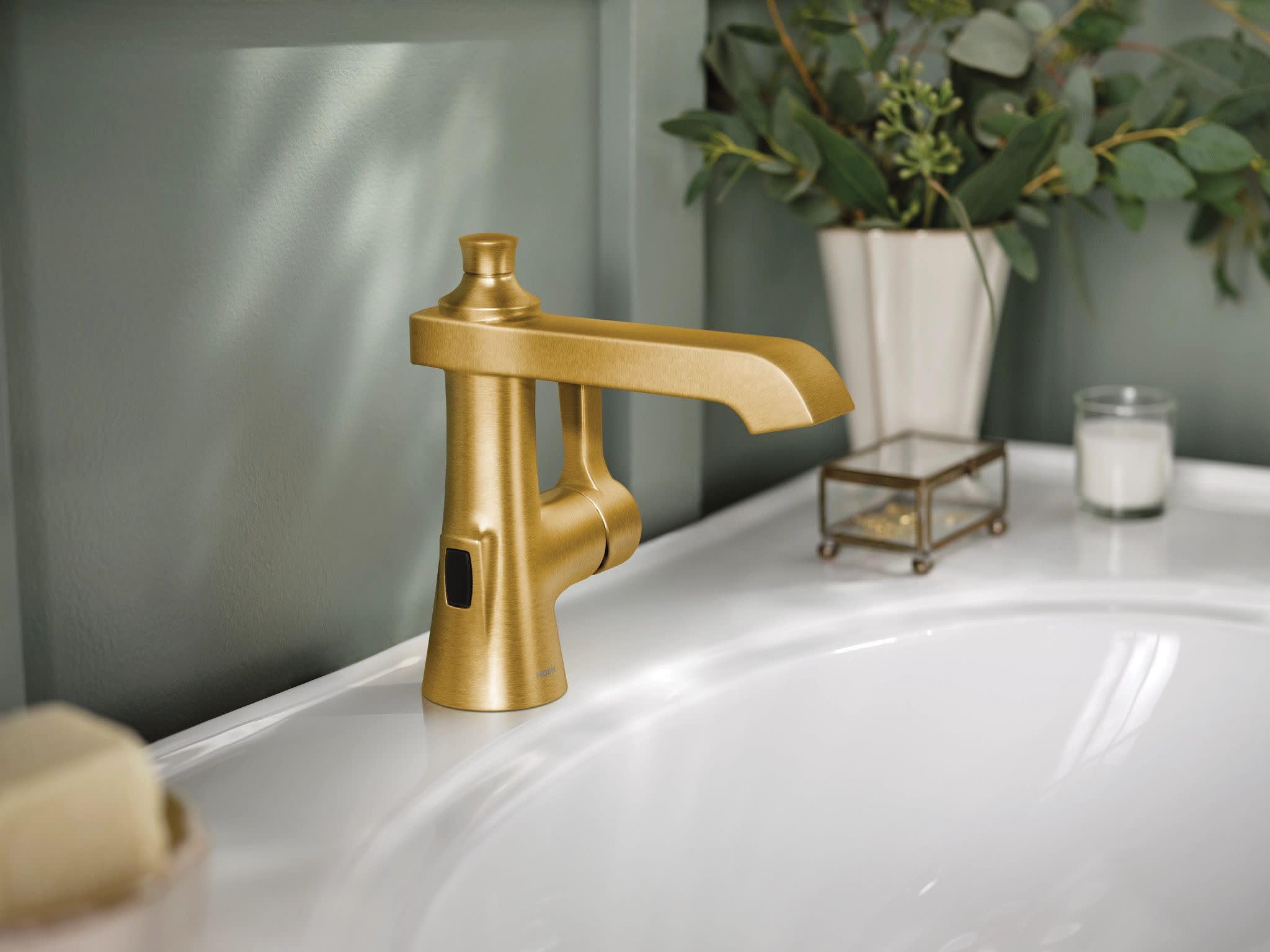 Brushed gold single-handle bathroom faucet with curved spout and motion sensor mounted on white sink.