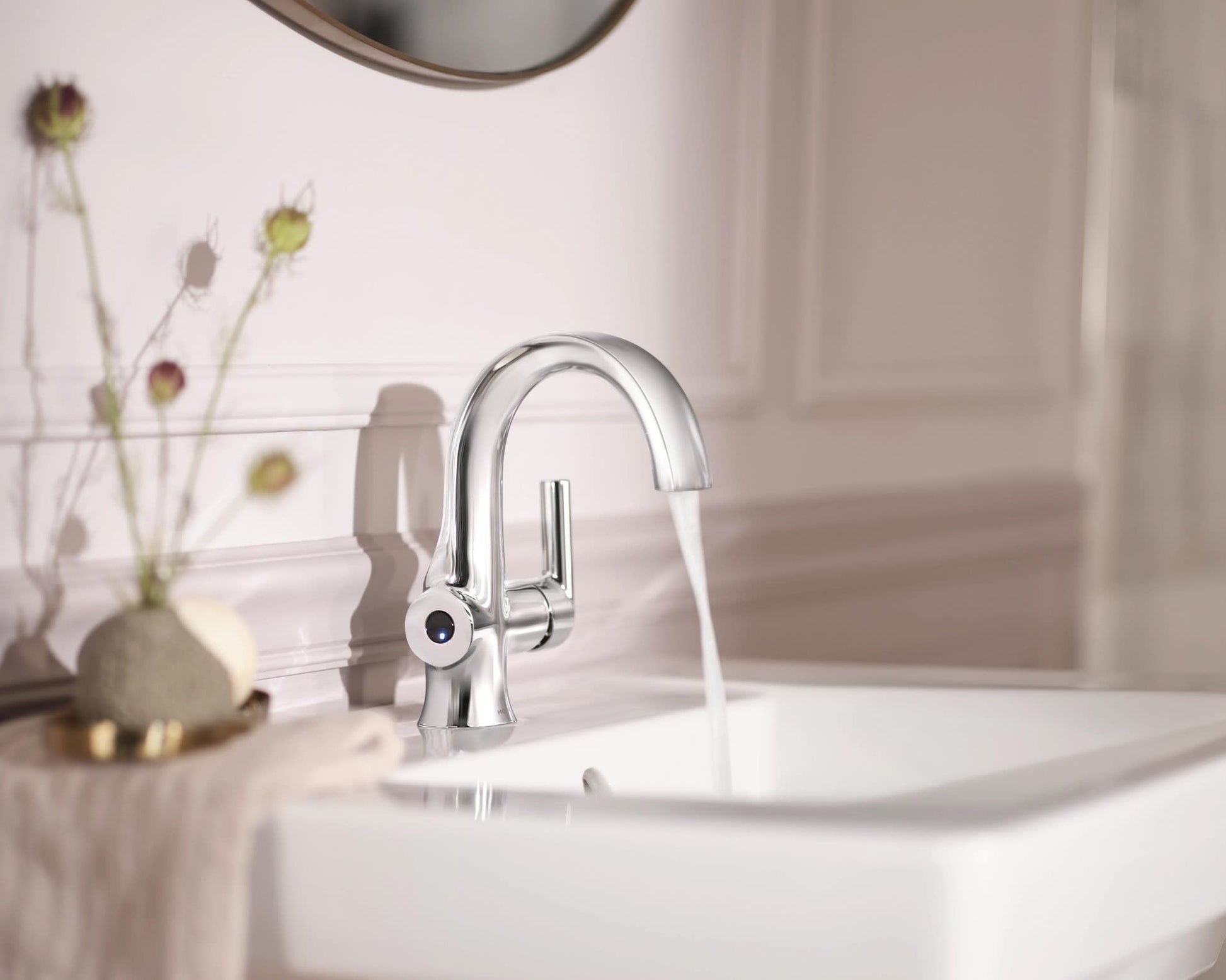 Chrome single-handle bathroom faucet with curved spout and motion-sensor technology installed on white sink.