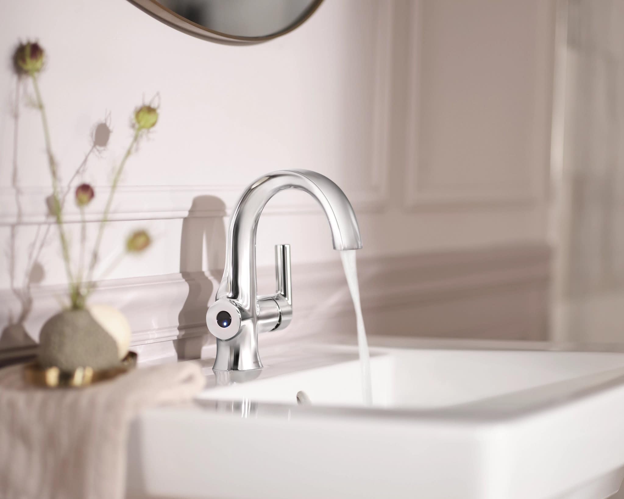 Chrome single-handle bathroom faucet with curved spout and motion-sensor technology installed on white sink.